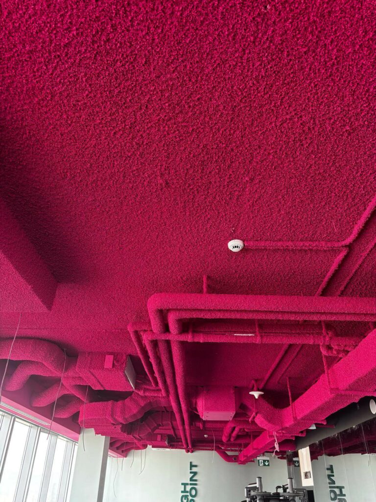 Plafond de salle de sport dont gaines de ventilation et canalisations sont traitées en projection acoustique rose framboise, illustration de la surface développée facturée