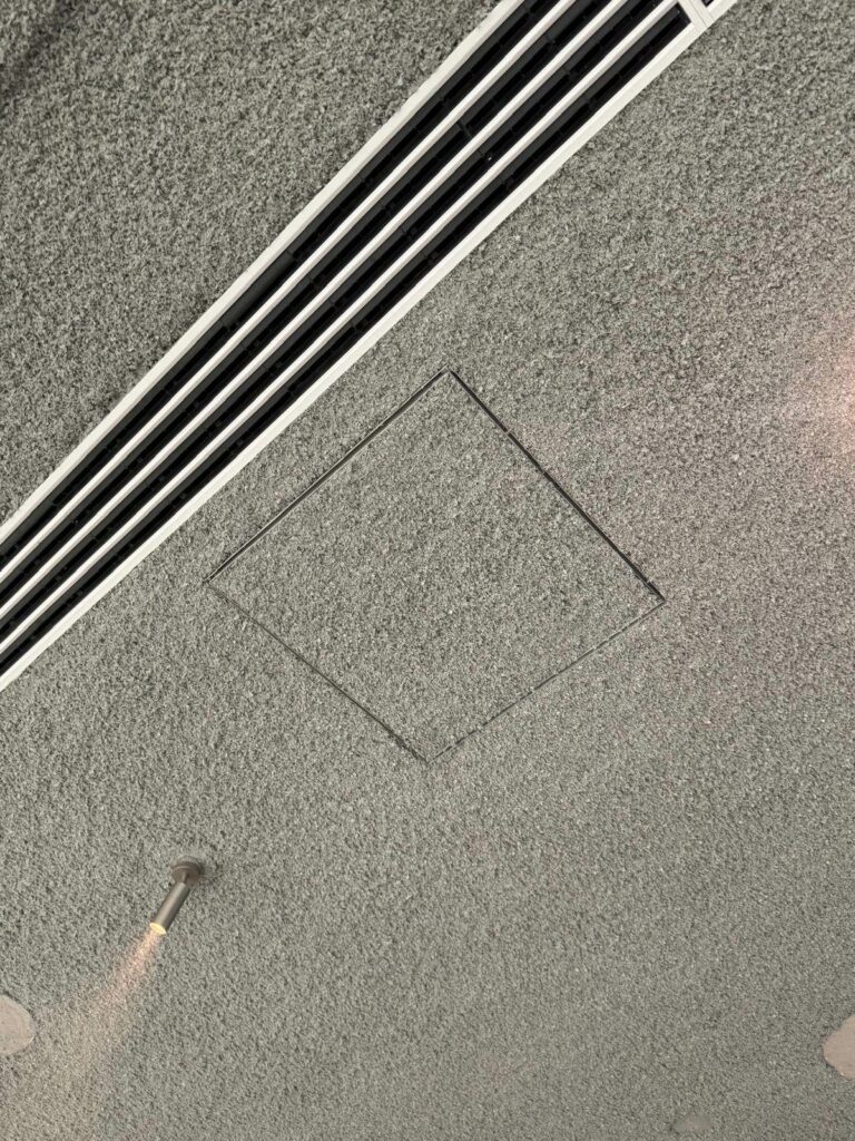 Trappe de visite et diffuseur linéaire de ventilation intégrés dans l'épaisseur d'un plafond acoustique projeté gris