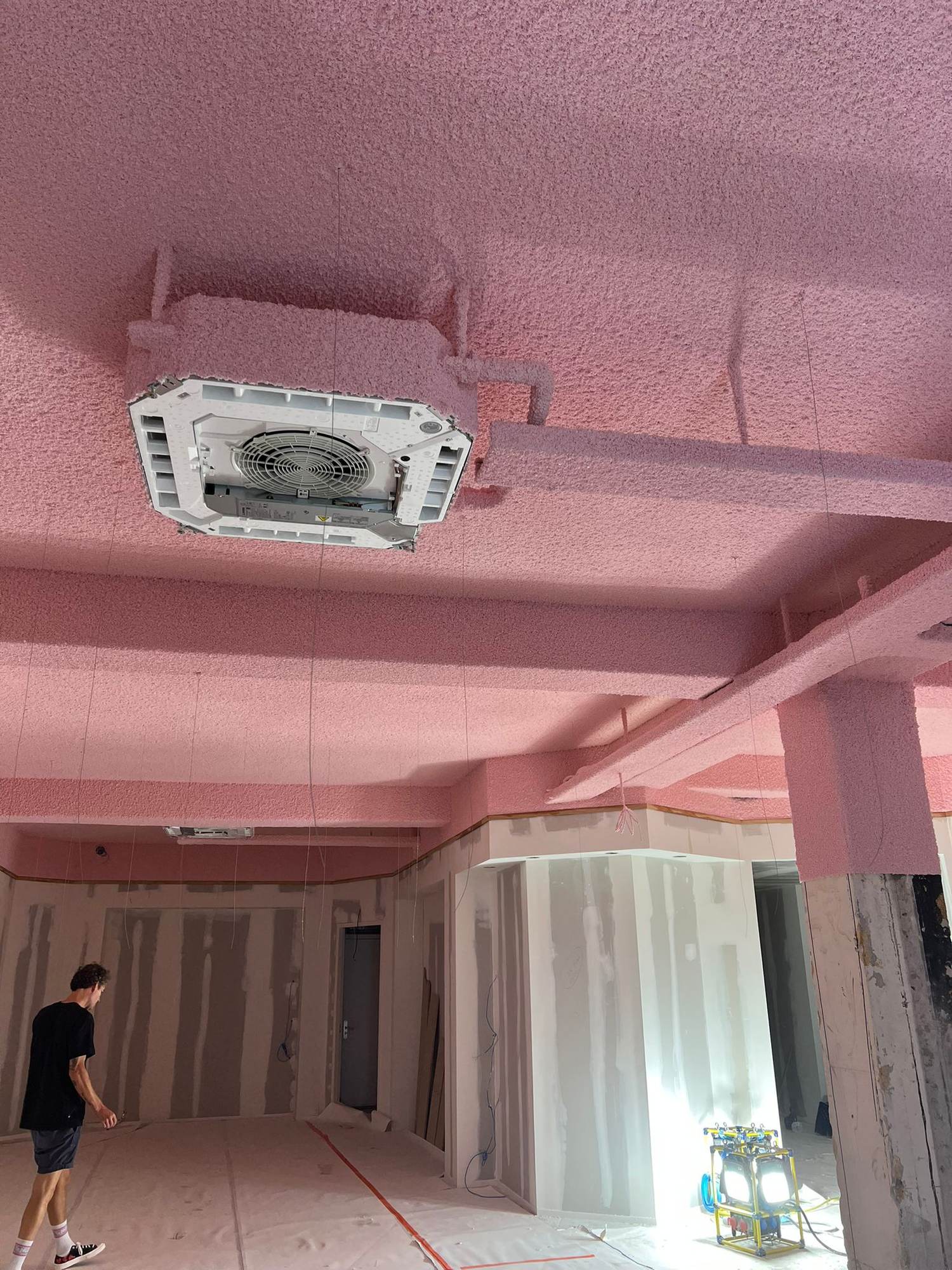 Projection acoustique continue sur dalle béton, poutres et cassette de climatisation dans un chantier de bureaux