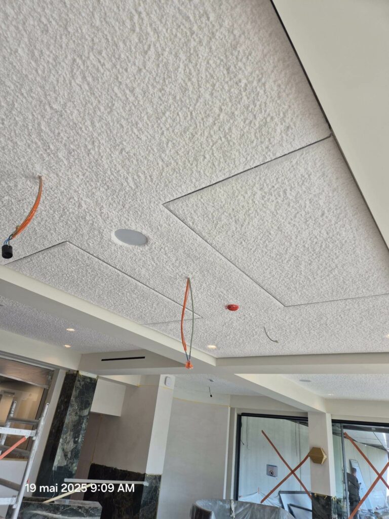 Texture grenue d'un plafond acoustique projeté blanc en cours de chantier, surface poreuse qui produit le coefficient d'absorption acoustique